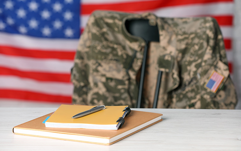 Camo jacket hanging over chair and notebooks on table